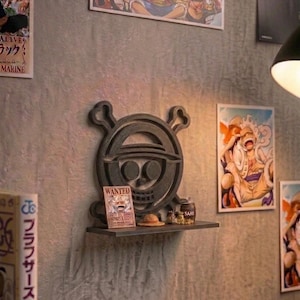 Può includere: Una mensola da parete grigio scuro con un design a teschio e ossa incrociate, un poster "Wanted" e accessori in miniatura. La mensola è montata su una parete grigia strutturata, con poster di anime sullo sfondo.
