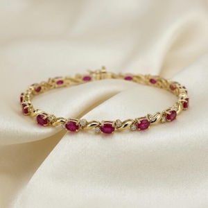 May include: A gold bracelet featuring a series of oval-cut red rubies alternating with small round white diamonds. The metal links between the gemstones have a smooth, polished finish, and the piece includes a secure clasp mechanism.