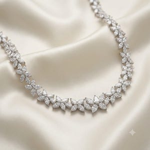 May include: A silver-toned necklace featuring a continuous chain of interconnected floral motifs. Each flower is composed of multiple marquise-cut clear stones arranged in a petal pattern, creating a sparkling, symmetrical design throughout the piece.