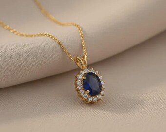 May include: A gold necklace featuring an oval-shaped deep blue sapphire pendant surrounded by a halo of small, clear, round-cut white stones. The pendant is suspended from a delicate gold chain, creating a classic and elegant jewelry piece.