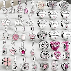 Puede incluir: Una colección de abalorios de plata con diversos diseños, incluyendo corazones, flores y colgantes con textos como "Madre" y "Hermana". Algunos abalorios presentan detalles rosas y brillantes.