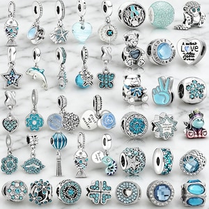 May include: A selection of silver charms in various designs, including fish, stars, hearts, and bears, in shades of blue and silver. Some charms feature clear crystals and engraved details. The charms are designed for bracelets or necklaces.