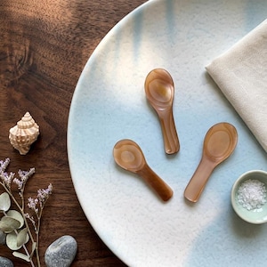 May include: A white ceramic mug with a black handle and the text "But First, Coffee" in a black, bold font. The mug is on a white surface.