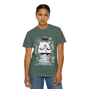 Op de afbeelding: Groen t-shirt met een eigenzinnige kattenillustratie. De witte kat heeft een strenge uitdrukking en draagt een hoed. Tekst bevat "Mysterious Cat", "Quirky" en "Watch Out".