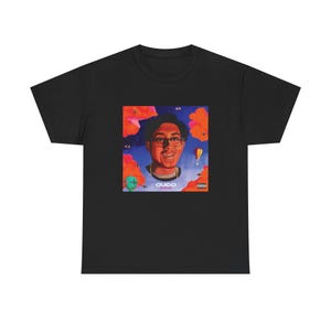 May include: Black t-shirt featuring a colorful graphic of a person wearing glasses, surrounded by orange and blue clouds, eyes, and a hot air balloon. The graphic includes the text "CUCO" and "Paraiso".
