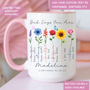 May include: White ceramic mug with a pink handle and rim, featuring floral illustrations and the text "God Says You Are." The mug includes the name "Madeline" and the date "02.06.26." Additional text includes "unique," "strong," "beautiful," "forgiven," "precious," and "chosen."