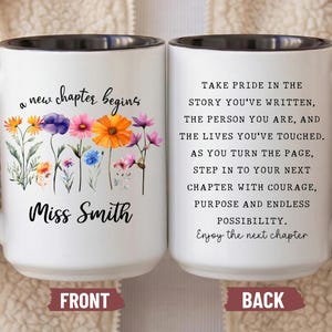 May include: A white ceramic mug with a black handle and interior. The front features colorful watercolor wildflowers and the text 'a new chapter begins Miss Smith'. The back displays the text 'TAKE PRIDE IN THE STORY YOU'VE WRITTEN... Enjoy the next chapter'.