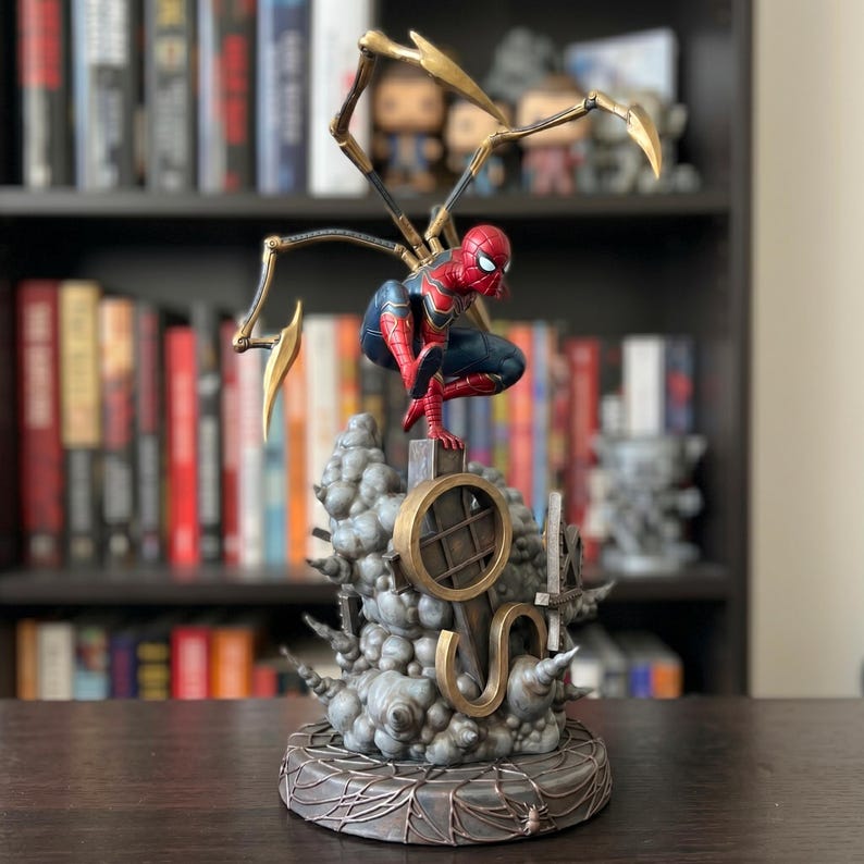 Op de afbeelding: Een Spider-Man actiefiguur in een rood en blauw pak, gehurkt op een grijze, rookachtige basis. Het figuur heeft vier gouden mechanische spinnenpoten op de rug, een cirkelvormig goudkleurig frame en een ronde basis met een spinnenwebpatroon.