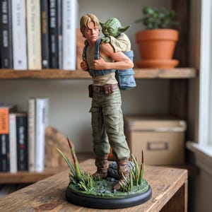 Pode incluir: Uma estatueta detalhada de um personagem humano loiro com regata bege e calças cargo verde-oliva, carregando uma pequena criatura verde de orelhas pontudas numa mochila azul, sobre uma base circular com relva verde.