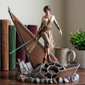 May include: A detailed collectible figurine of a character with short brown hair, wearing a tan sleeveless tunic, brown pants, and arm wraps. The figure holds a thin blue lightsaber and stands on a base featuring a metallic structure and debris.