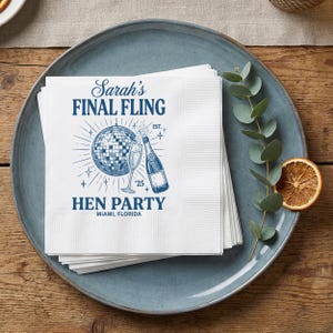 May include: White paper napkins with a blue design featuring a disco ball, champagne bottle, and the text "Sarah's Final Fling Hen Party Miami, Florida". The napkins are stacked on a blue plate.