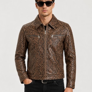 May include: A brown snakeskin-patterned jacket with a zipper closure and two chest pockets. The jacket has a collared neckline and is worn with black jeans and a black belt. The person in the image is wearing sunglasses.