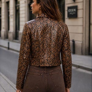 Peut inclure: Veste marron &agrave; motif peau de serpent avec col crant&eacute; et manches longues. Le blouson est associ&eacute; &agrave; un jean marron. La photo, prise de dos, met en valeur la texture et le style de l'ensemble.