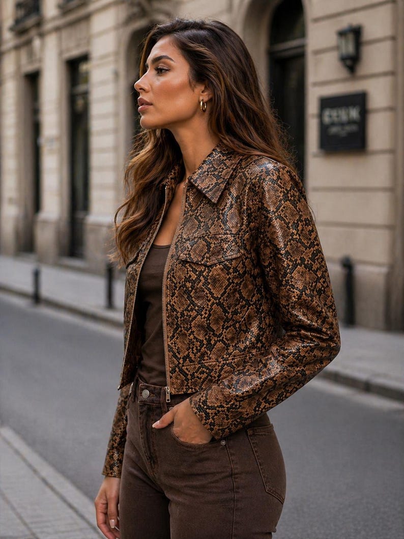 Peut inclure: Veste marron et noire &agrave; motif peau de serpent, avec un col et une fermeture &eacute;clair. La veste a deux poches avant et est port&eacute;e avec un pantalon marron et un haut marron. La tenue est port&eacute;e &agrave; l'ext&eacute;rieur.