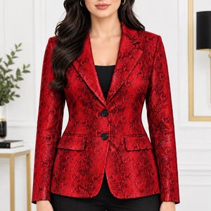 May include: A vibrant red blazer featuring a black snakeskin pattern, a notched lapel, long sleeves, and two black buttons down the front. The jacket includes two flap pockets at the waist and is worn over a simple black top and black trousers.