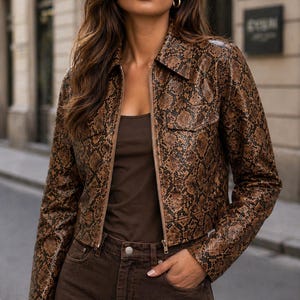 Peut inclure: Veste marron &agrave; motif peau de serpent avec un col et une fermeture &eacute;clair. La veste est associ&eacute;e &agrave; un d&eacute;bardeur marron et &agrave; un jean marron. La tenue est compl&eacute;t&eacute;e par des cr&eacute;oles dor&eacute;es.