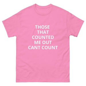 May include: A pink t-shirt with short sleeves, featuring the white text "THOSE THAT COUNTED ME OUT CANT COUNT". The shirt has a crew neck and a standard fit, suitable for casual wear.