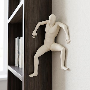 May include: A cream-colored, human-form sculpture is mounted on a dark brown wooden surface and a white wall. The sculpture is in a climbing pose, with arms and legs extended. The sculpture is a decorative item.