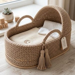 May include: A beige crocheted baby bassinet with a wooden base. The bassinet has a rounded hood and handles, and is filled with a cream-colored blanket and pillow. A tag reads "HANDMADE WITH LOVE".