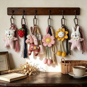 May include: A collection of handmade keychains hanging from a wooden rack. The keychains feature various designs, including a bear, strawberry, horse, flower, and bunny. Each keychain has a unique color scheme and decorative elements, such as tassels and embroidery.