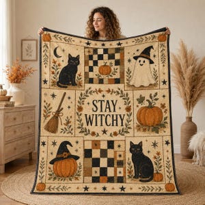 May include: A rectangular throw blanket featuring a cream background with a repeating Halloween-themed pattern. The design includes black cats, a ghost wearing a witch hat, pumpkins, a broom, and a checkerboard motif with the text STAY WITCHY.