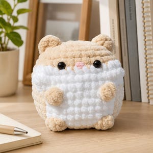 May include: A round, plush hamster toy crafted from soft, textured yarn. The figure features a light tan upper body and a white lower section, with two small rounded ears, black bead eyes, and a tiny pink stitched nose on its face.