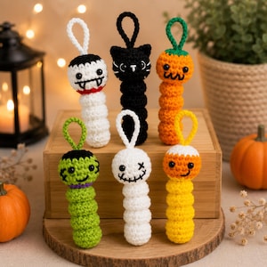 May include: Six crocheted Halloween ornaments featuring a vampire, a black cat, a pumpkin, a green monster, a ghost, and a candy corn. Each figure has a loop at the top for hanging and is crafted with yarn in distinct colors and facial expressions.