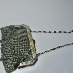 May include: Antique silver mesh purse with a chain handle. The purse has a rectangular frame and a delicate, woven mesh body. Small silver beads adorn the bottom edge. The chain handle is also silver.