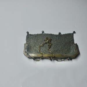 May include: A vintage silver mesh purse with a rectangular shape. The purse features a fine, woven mesh body, a silver-toned frame, and a delicate chain strap. Small silver beads adorn the top edge. A classic accessory.