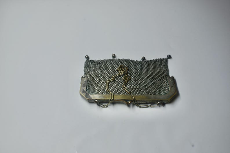 May include: A vintage silver mesh purse with a rectangular shape. The purse features a fine, woven mesh body, a silver-toned frame, and a delicate chain strap. Small silver beads adorn the top edge. A classic accessory.