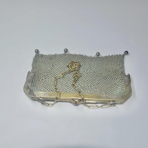 May include: A vintage silver mesh purse with a rectangular shape. The purse features a delicate chain handle and a metal frame. The mesh is finely woven, and the purse has a classic, elegant design. The purse is a light silver color.