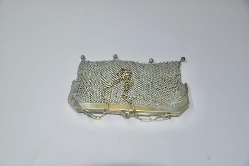 May include: A vintage silver mesh purse with a rectangular shape. The purse features a delicate chain handle and a metal frame. The mesh is finely woven, and the purse has a classic, elegant design. The purse is a light silver color.