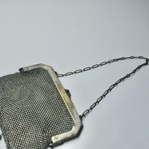 May include: A vintage silver mesh purse with a chain handle. The purse has a rectangular frame and small decorative beads at the bottom. The mesh is tightly woven, and the chain is dark in color.