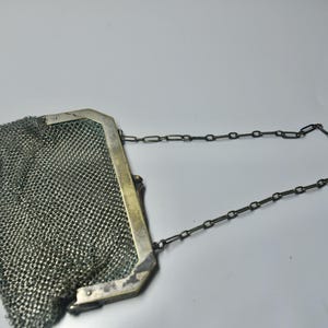 May include: A vintage silver mesh purse with a rectangular frame and a chain handle. The purse has a delicate, woven mesh body and small decorative beads at the bottom. The frame is a light silver color.
