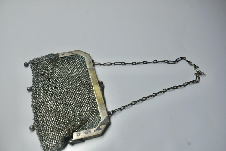 May include: A vintage silver mesh purse with a rectangular frame and a chain handle. The purse has a delicate, woven mesh body and small decorative beads at the bottom. The frame is a light silver color.