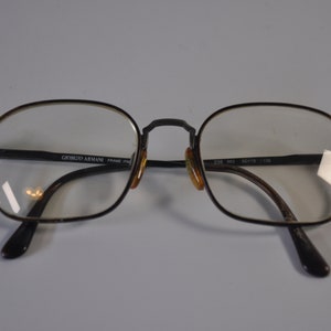 May include: Black metal frame eyeglasses with clear lenses. The frame has the text "Giorgio Armani Frame Italy" on the left arm and "238 903 52/18 135" on the right arm.