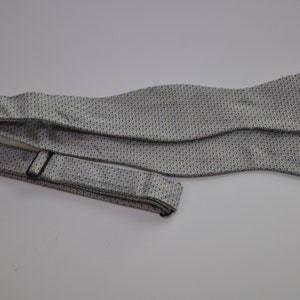 May include: A white bow tie with a black patterned design. The bow tie is made of a silky material and has a long, adjustable strap.