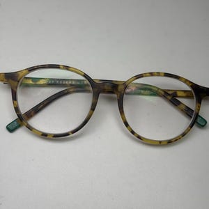 May include: Tortoise shell eyeglasses with round frames and green accents. The arms of the glasses are labeled "GOOD ROGERS U.S.A."