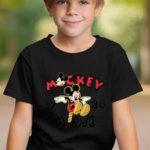 May include: Black t-shirt with a Mickey Mouse graphic. The design features the word "Mickey" in red, the year "1924", and the word "Mouse" in black. Mickey Mouse is shown in his classic pose, with yellow shoes and red shorts.