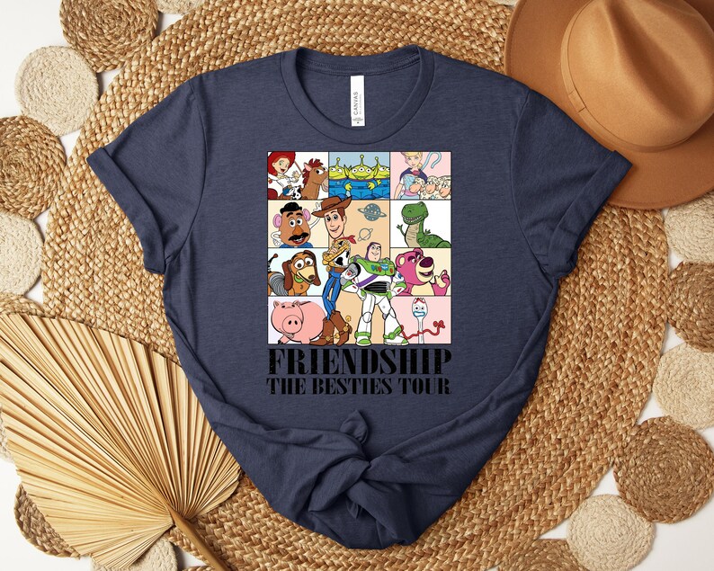 Puede incluir: Camiseta azul marino con un gr&aacute;fico colorido de personajes de dibujos animados en un patr&oacute;n de cuadr&iacute;cula. El texto "FRIENDSHIP THE BESTIES TOUR" est&aacute; impreso debajo. La camiseta tiene cuello redondo y mangas cortas.