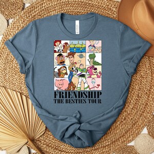 Puede incluir: Una camiseta azul con un gr&aacute;fico de personajes de dibujos animados en una cuadr&iacute;cula. El texto "FRIENDSHIP THE BESTIES TOUR" est&aacute; impreso en negro. La camiseta est&aacute; hecha de un material suave. Es una prenda informal.