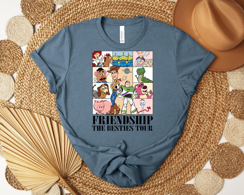 Puede incluir: Una camiseta azul con un gr&aacute;fico de personajes de dibujos animados en una cuadr&iacute;cula. El texto "FRIENDSHIP THE BESTIES TOUR" est&aacute; impreso en negro. La camiseta est&aacute; hecha de un material suave. Es una prenda informal.