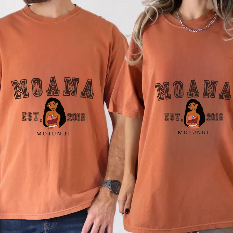 Pu&ograve; includere: Due magliette arancioni con la scritta "MOANA" a blocchi. Sotto, un personaggio dei cartoni animati, la scritta "EST. 2016" e la parola "MOTUNUI".