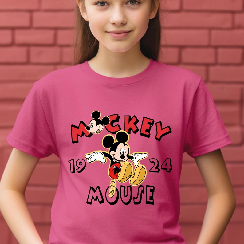 May include: A magenta t-shirt with a Mickey Mouse graphic. The design features the words "Mickey Mouse" in black and red, and the numbers "19" and "24". The t-shirt is being worn by a person.