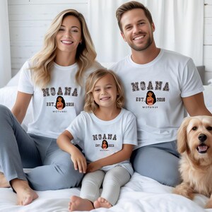 Pu&ograve; includere: Una famiglia indossa magliette bianche abbinate con la parola "MOANA" in un font universitario. Le magliette presentano anche una grafica di una donna e il testo "EST. 2018 MOTUNUI". Un cane golden retriever &egrave; anche nell'immagine.