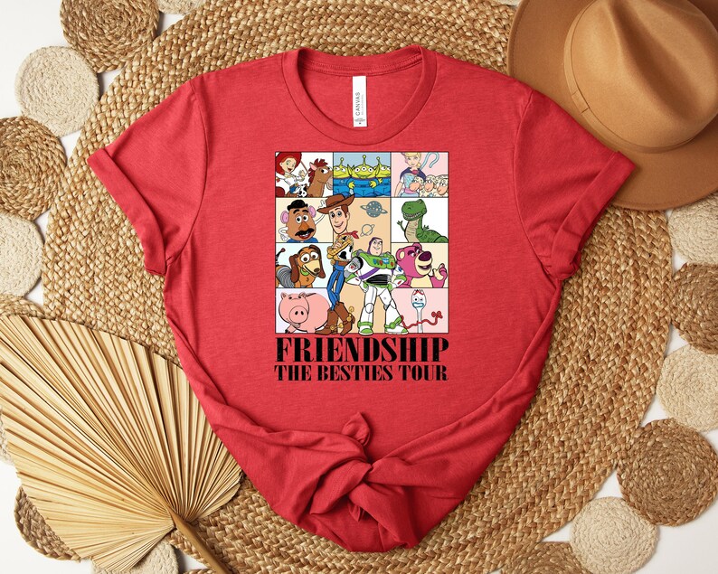 Puede incluir: Camiseta roja con un dise&ntilde;o gr&aacute;fico colorido de personajes de dibujos animados. El dise&ntilde;o est&aacute; dividido en cuadrados y contiene el texto "FRIENDSHIP THE BESTIES TOUR". La camiseta est&aacute; hecha de un material suave y tiene un cuello redondo cl&aacute;sico.