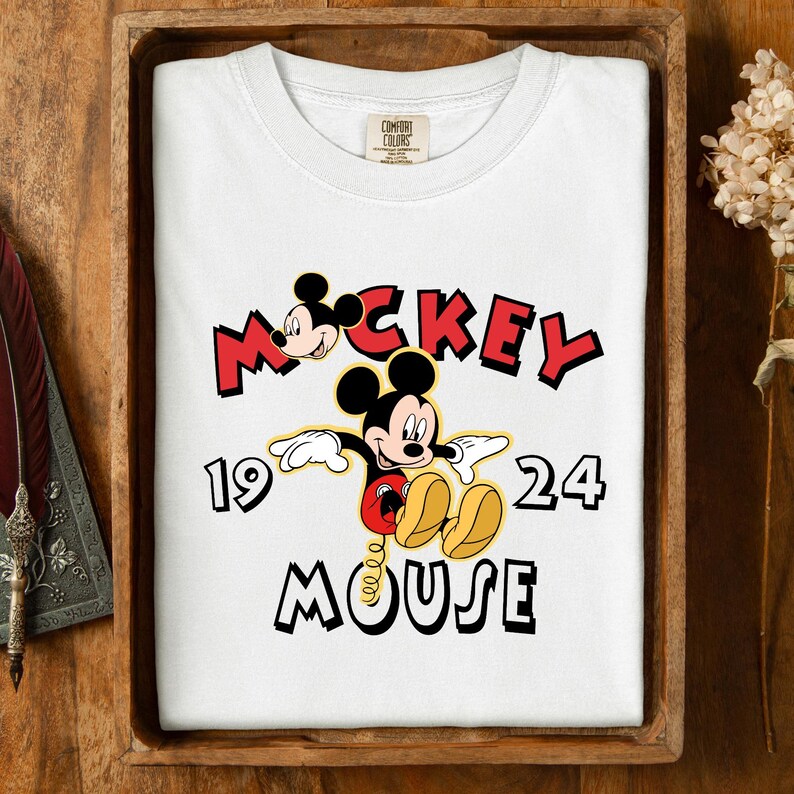 May include: White t-shirt with a Mickey Mouse graphic and the text "Mickey Mouse 1924" in red and black. The shirt is presented in a wooden tray.