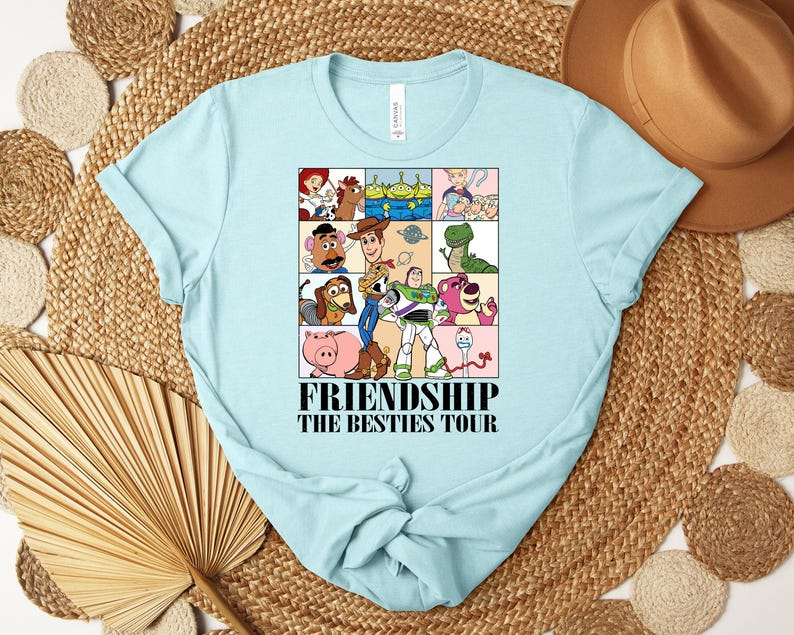 Puede incluir: Camiseta azul claro con un dise&ntilde;o de personajes de dibujos animados en una cuadr&iacute;cula. El texto "FRIENDSHIP THE BESTIES TOUR" est&aacute; impreso debajo. La camiseta es de material suave y tiene cuello redondo. Una prenda casual.