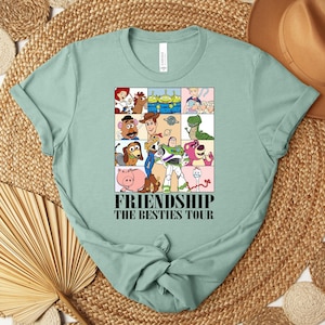 Puede incluir: Camiseta verde claro con un gr&aacute;fico colorido de personajes de dibujos animados en una cuadr&iacute;cula. El gr&aacute;fico incluye el texto "FRIENDSHIP THE BESTIES TOUR". La camiseta est&aacute; hecha de un material suave y tiene un cuello redondo cl&aacute;sico.
