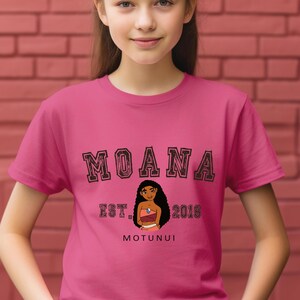 Pu&ograve; includere: Una maglietta rosa con la scritta "MOANA" in nero, con contorno. Sotto, un'illustrazione di un personaggio dei cartoni animati, con il testo "EST. 2016" e "MOTUNUI". La maglietta &egrave; indossata da una persona.